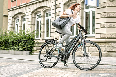 A woman rides through the city center on a Winora bicycle with a handbag under her arm.